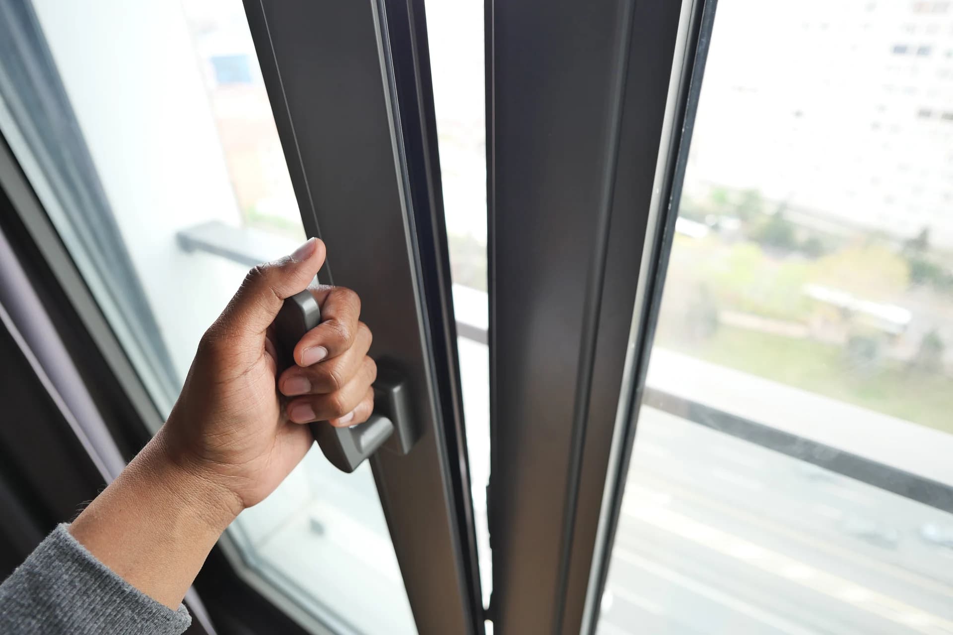 Hand opening an anthracite grey aluminium window with a city view in Briton Ferry